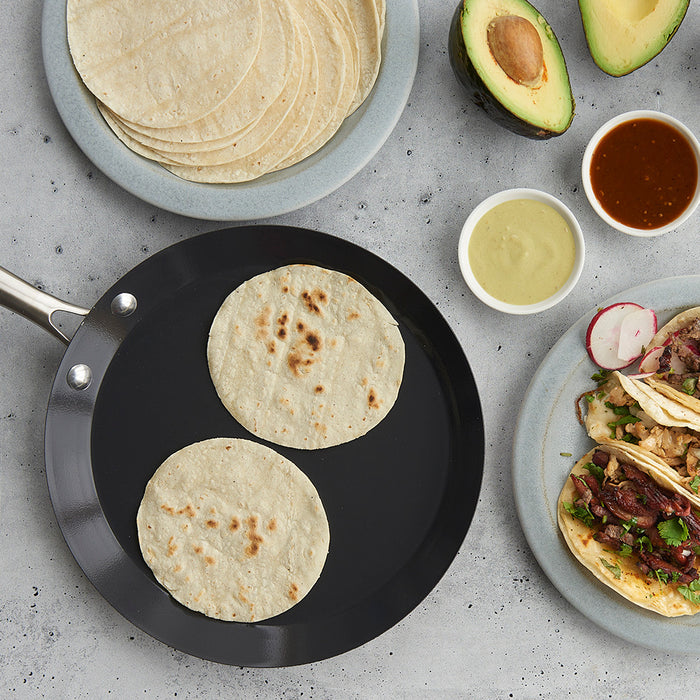 Crepe pan with warm tortillas next to plated tacos
