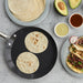 Crepe pan with warm tortillas next to plated tacos