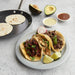 Crepe pan with a golden crepe next to plated tacos