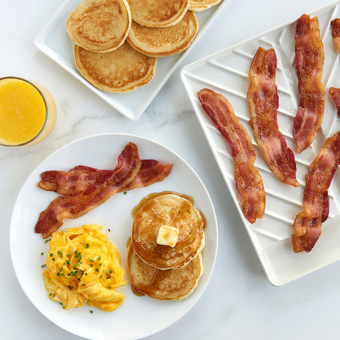 Slanted bacon tray with crispy bacon next to pancakes and eggs